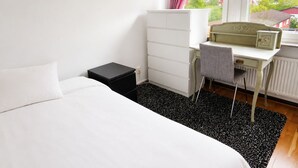 A hotel room with a bed, a desk, a chair, a small black nightstand, and a window with a view of buildings. - Room-elegant Central Apartment Room in A (Kista)