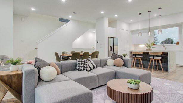 A modern living room with a sectional sofa, a round coffee table, and a dining area with a kitchen in the background.