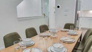 A dining table set with plates, glasses, and cutlery in a modern room with chairs and a view of a kitchen.