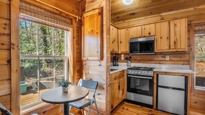 A wooden cabin interior with a kitchen, dining area, and a large window.