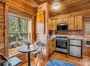 A wooden cabin interior with a kitchen, dining area, and a large window.