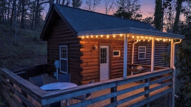 A wooden cabin with a deck, a door, and a small window.