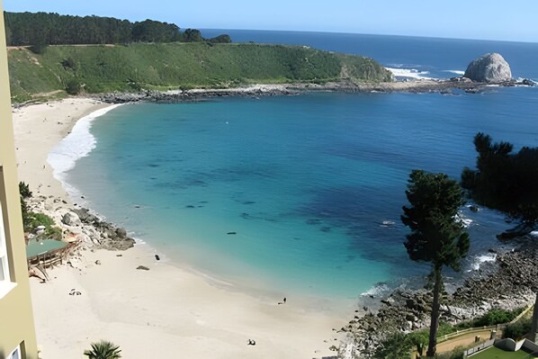 Une plage cĂŽtiĂšre aux eaux turquoise et limpides, avec un rivage sablonneux et une grande formation rocheuse.