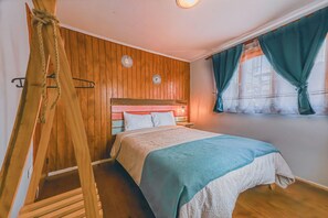 Une chambre avec un mur recouvert de lambris en bois, un lit avec une couvre-lit blanche et bleue, et une fenĂȘtre ornĂ©e de rideaux turquoise.