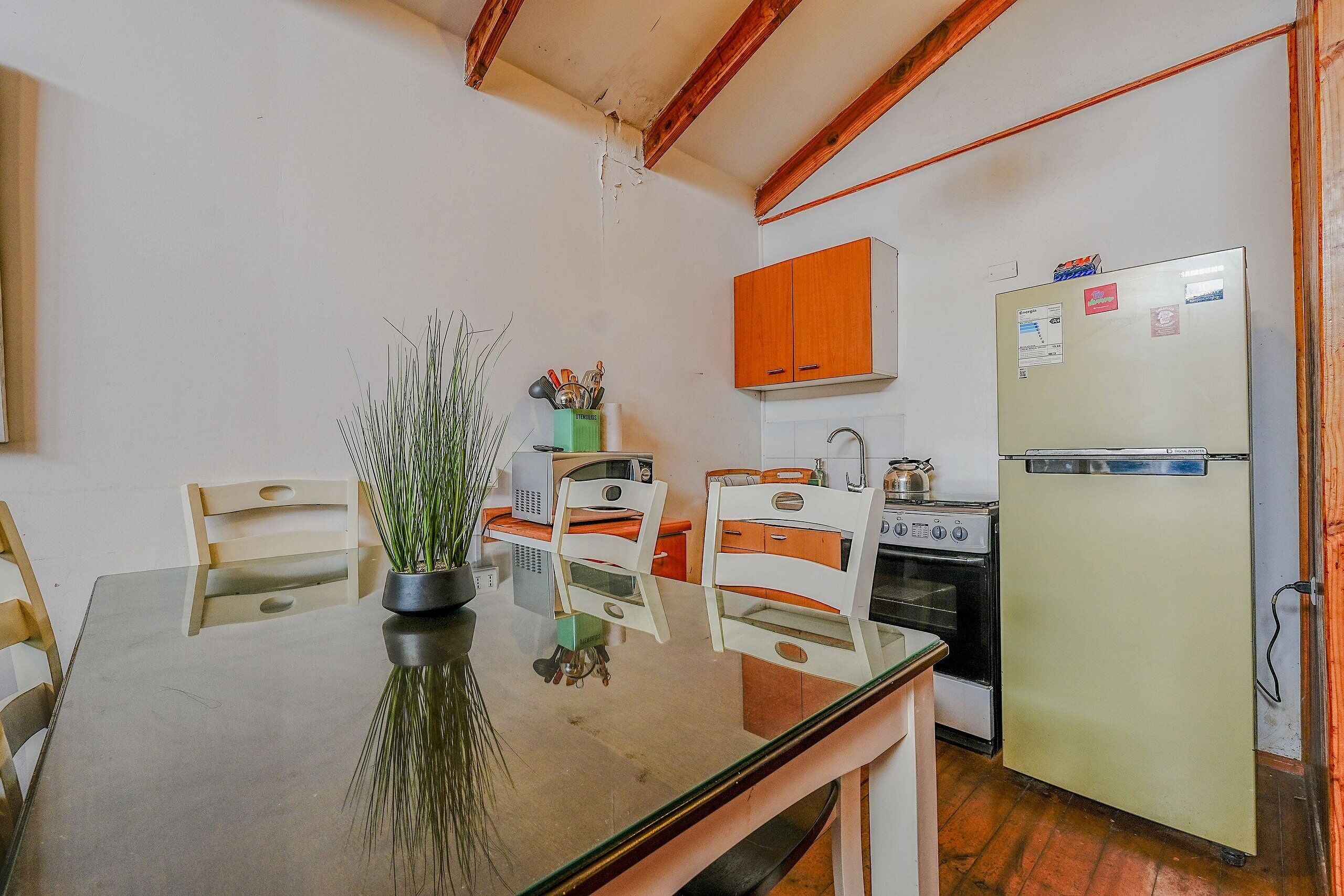 Uma cozinha com mesa de vidro, cadeiras, geladeira, forno e armários de madeira.
