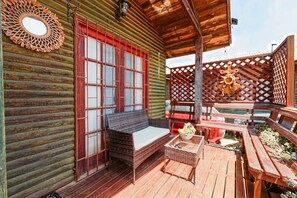 Une cabane en bois avec un porche couvert, un canapé en osier, une table en verre et un banc en bois.