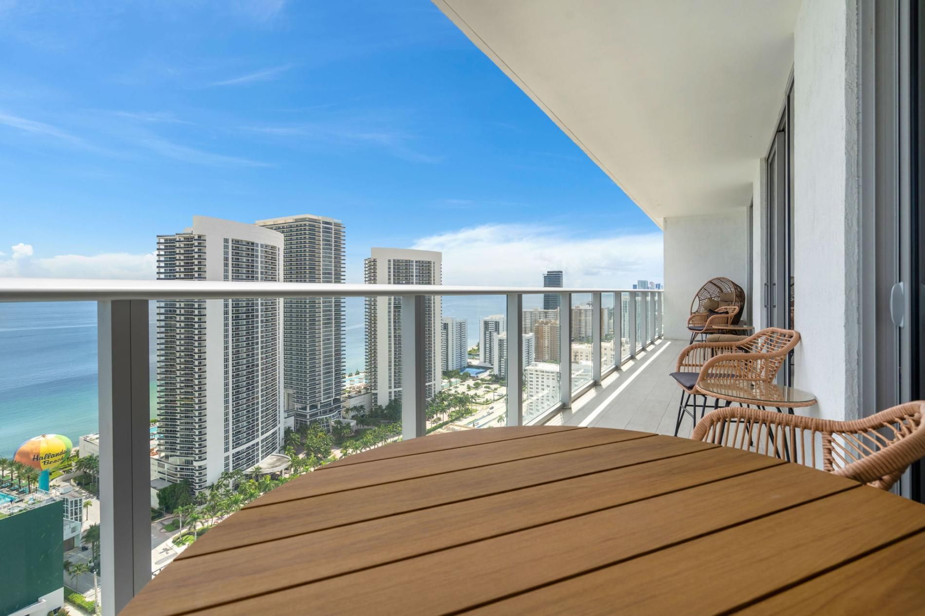 Un balcón con una mesa de madera y sillas de mimbre, con vistas a la ciudad y al océano.