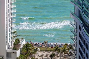 Vista de una playa desde un hotel de gran altura con balcones que dan al océano, palmeras y sillas de playa.