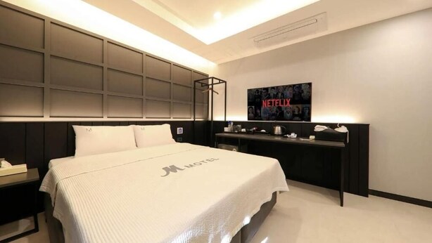 A modern hotel room with a large bed, a desk with a computer, and a wall-mounted TV.