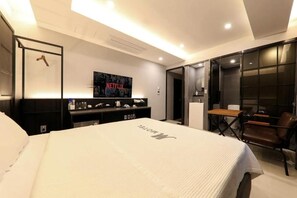 Una habitación de hotel moderna con una cama grande, un televisor montado en la pared, un escritorio con una silla y una puerta corredera que da al baño.