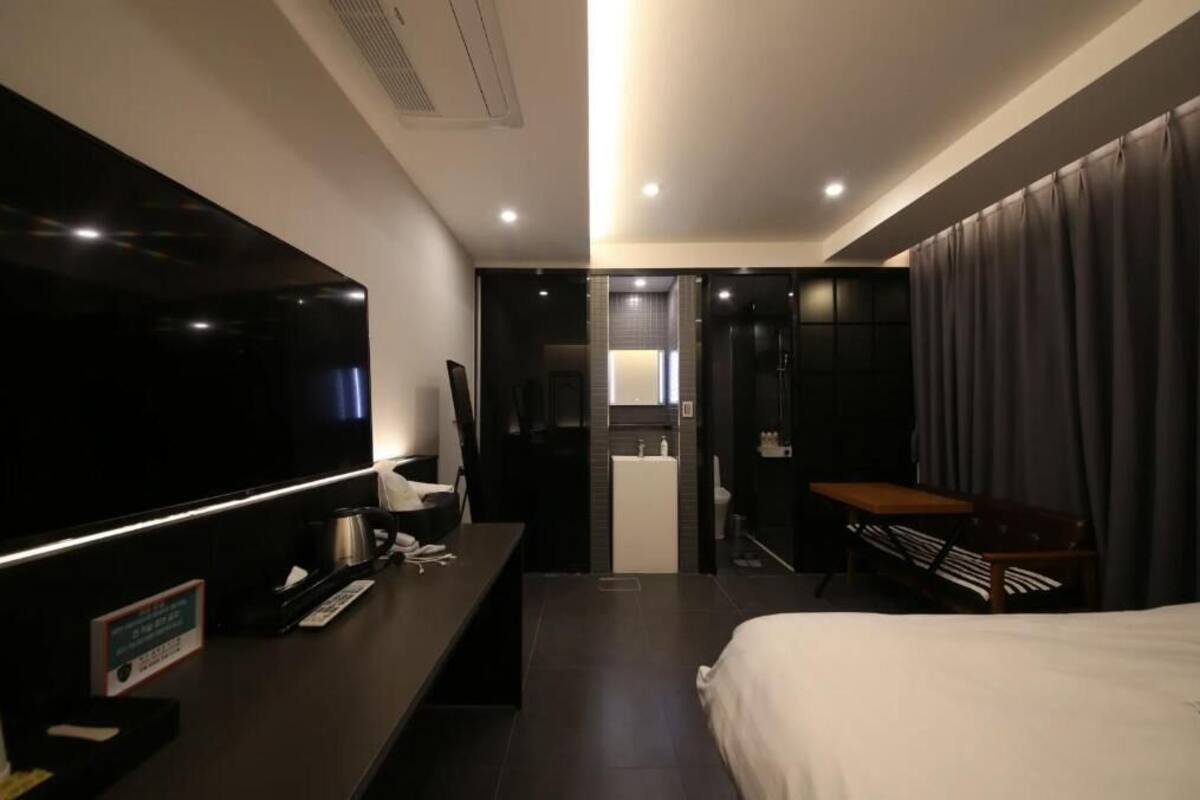 Et moderne hotelværelse med et stort fladskærms-tv, et skrivebord med telefon, en seng og et lille bord.