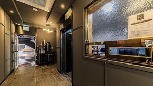 A hotel corridor with a reception desk, a seating area, and a view through a textured glass window.