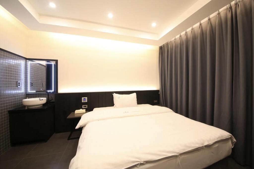 A hotel room with a bed, a bedside table, a nightstand, a mirror, and a bathroom with a sink and mirror.