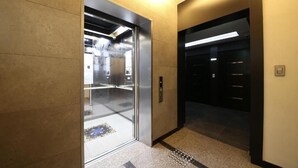 An elevator with a metallic interior and a glass door, a control panel, and a tiled floor.