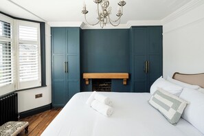 A bedroom with a large bed, a fireplace, and a window with blinds. - Charming 4BR Home with Garden and BBQ (Greater London)