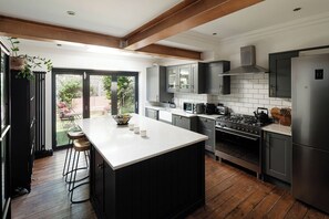 A modern kitchen with a large island, stainless steel appliances, and a view to an outdoor patio. - Charming 4BR Home with Garden and BBQ (Greater London)