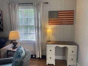 Ein Zimmer mit Fenster, Vorhängen, einer Lampe, einem Schreibtisch und einer US-amerikanischen Flagge.