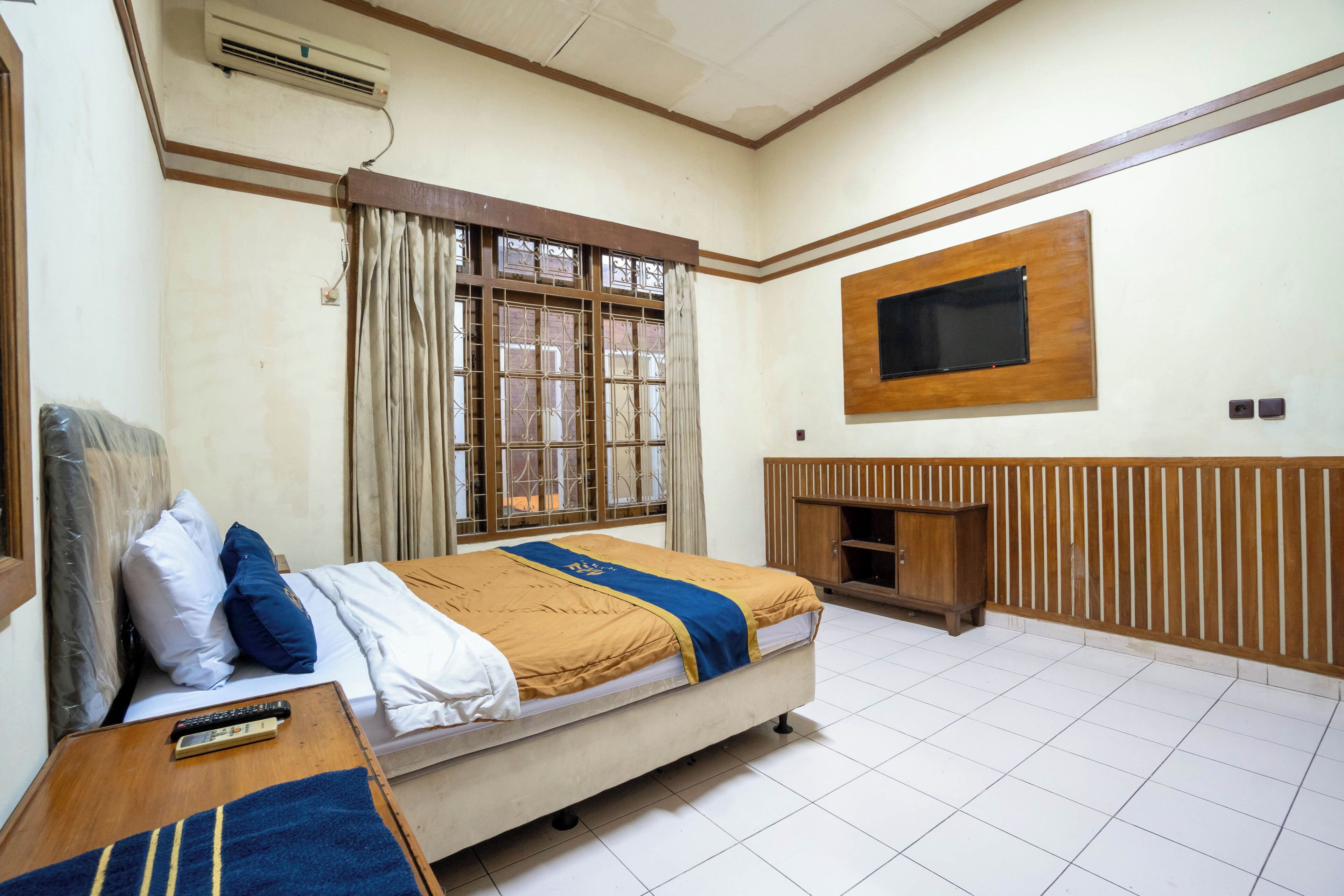 Una habitación con una cama, un televisor en la pared, una ventana con cortinas y un armario de madera.