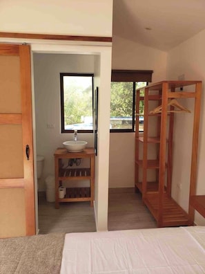 A bedroom with a bed, a wooden wardrobe, a bathroom with a sink and toilet, and a window with a view of trees. - Private room with pool, walking distance to beach (Playa Grande)