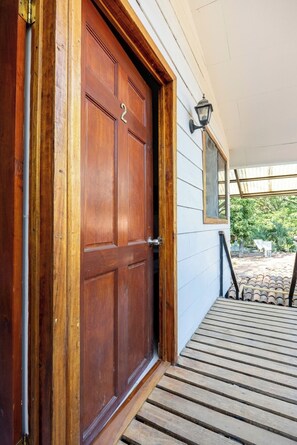 A wooden front door with a number plate, a porch with wooden steps, and a wall-mounted lantern. - Private room with pool, walking distance to beach (Playa Grande)