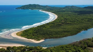 Un paisaje costero con una playa, colinas boscosas y cielo despejado.