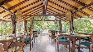 Un espacio de comedor al aire libre con mesas y sillas de madera, rodeado de abundante vegetación.
