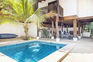Ein Pool mit Holzboden, Liegestühlen und einer Palme.