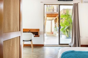Ein Hotelzimmer mit Bett, Schreibtisch mit Stuhl, einer Schiebetür zu einem Außenbereich und einem an der Wand befestigten Fernseher.