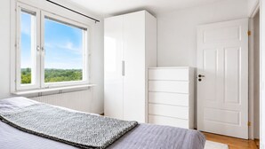 Un dormitorio con cama, armario, radiador y ventana con vistas a zonas verdes.