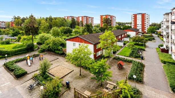 Zona residencial con un parque infantil, un pequeño edificio rojo y un sendero que lleva a una entrada con portón.