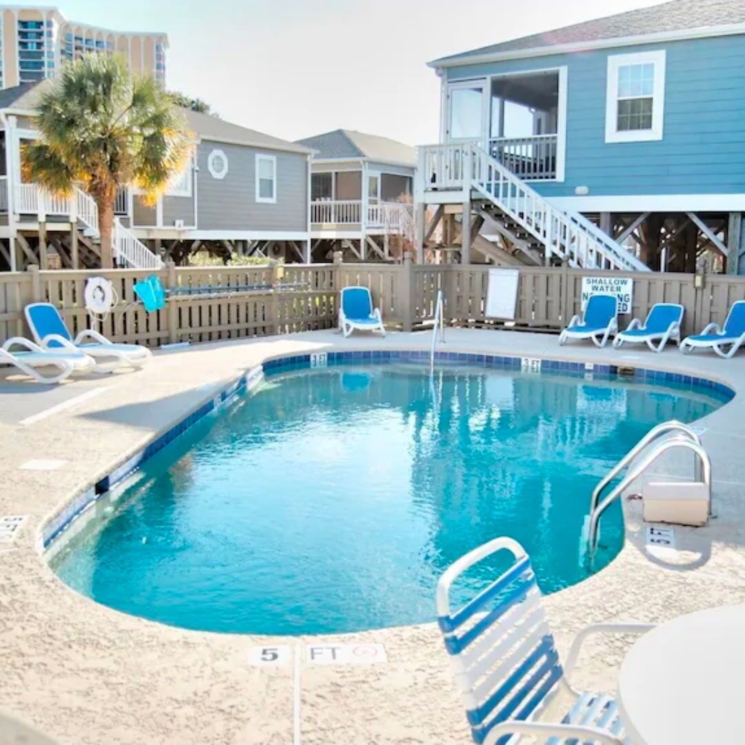 A swimming pool with lounge chairs, a wooden deck, and a sign indicating shallow water.