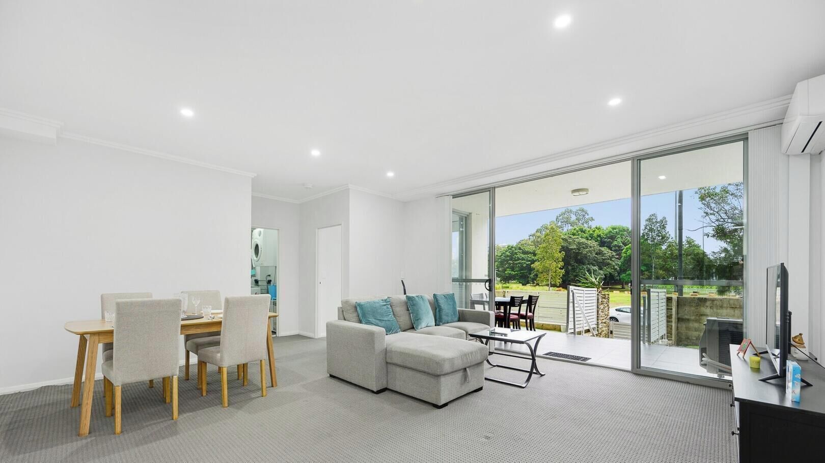 A modern living room with a dining area, a sofa, and a balcony with a view.