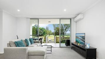 A modern living room with a grey sofa, teal cushions, a flat-screen TV, and a sliding glass door leading to an outdoor area.