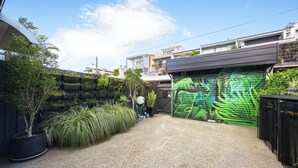 A residential garage with a green garage door, a gravel driveway, and a variety of potted plants and trees. - KozyGuru | Glebe | Chic Stay - Steps to Light Rail (Glebe)