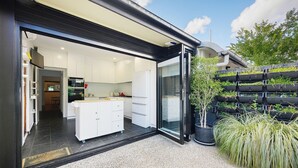 A modern kitchen with white cabinets and a glass door leading to a dining area. - KozyGuru | Glebe | Chic Stay - Steps to Light Rail (Glebe)