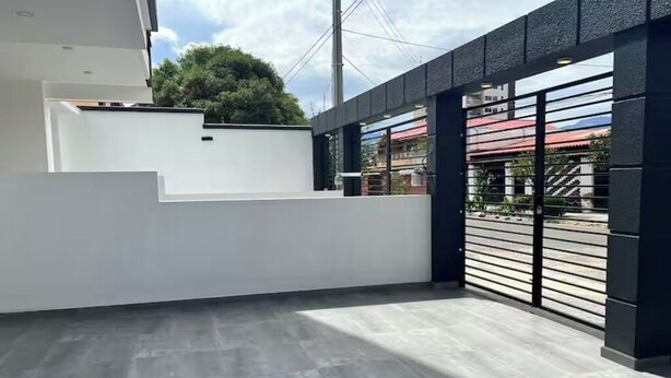 Un bâtiment moderne doté d’un toit plat, d’un mur blanc et d’un portail en métal noir.