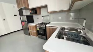 Une cuisine moderne avec des plans de travail blancs, des meubles en bois, un évier en acier inoxydable et un four encastré.