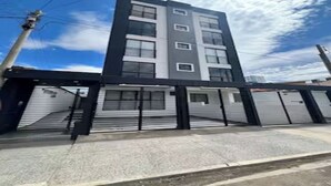Un immeuble à plusieurs étages, doté d’une architecture moderne, et dont le rez-de-chaussée est caractérisé par une série de portes de garage fermées.