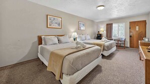 Una habitación de hotel con dos camas, un escritorio, una silla, una lámpara y una puerta.