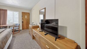 Una habitación de hotel con una cama, un televisor en una cómoda de madera, un escritorio con una silla y una ventana con cortinas.