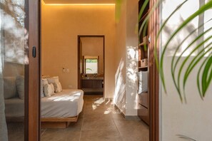 Ein Schlafzimmer mit Bett, ein Badezimmer mit Spiegel und Blick ins Freie.