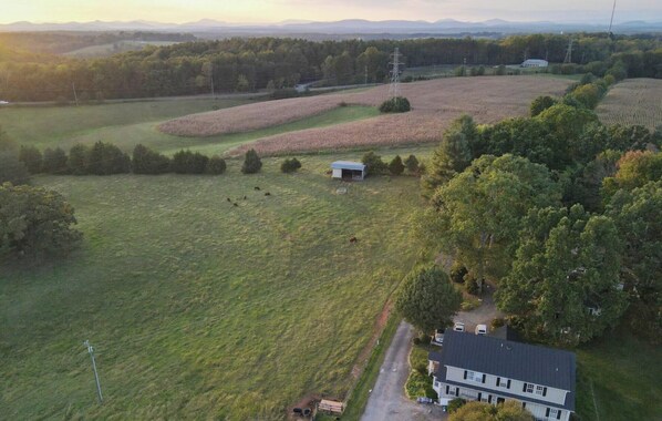 An aerial view of a rural property with a large field, a small building, and a house with a dark roof.