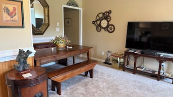 A living room with a wooden dining table, benches, a TV stand with books, a clock, and a mirror.
