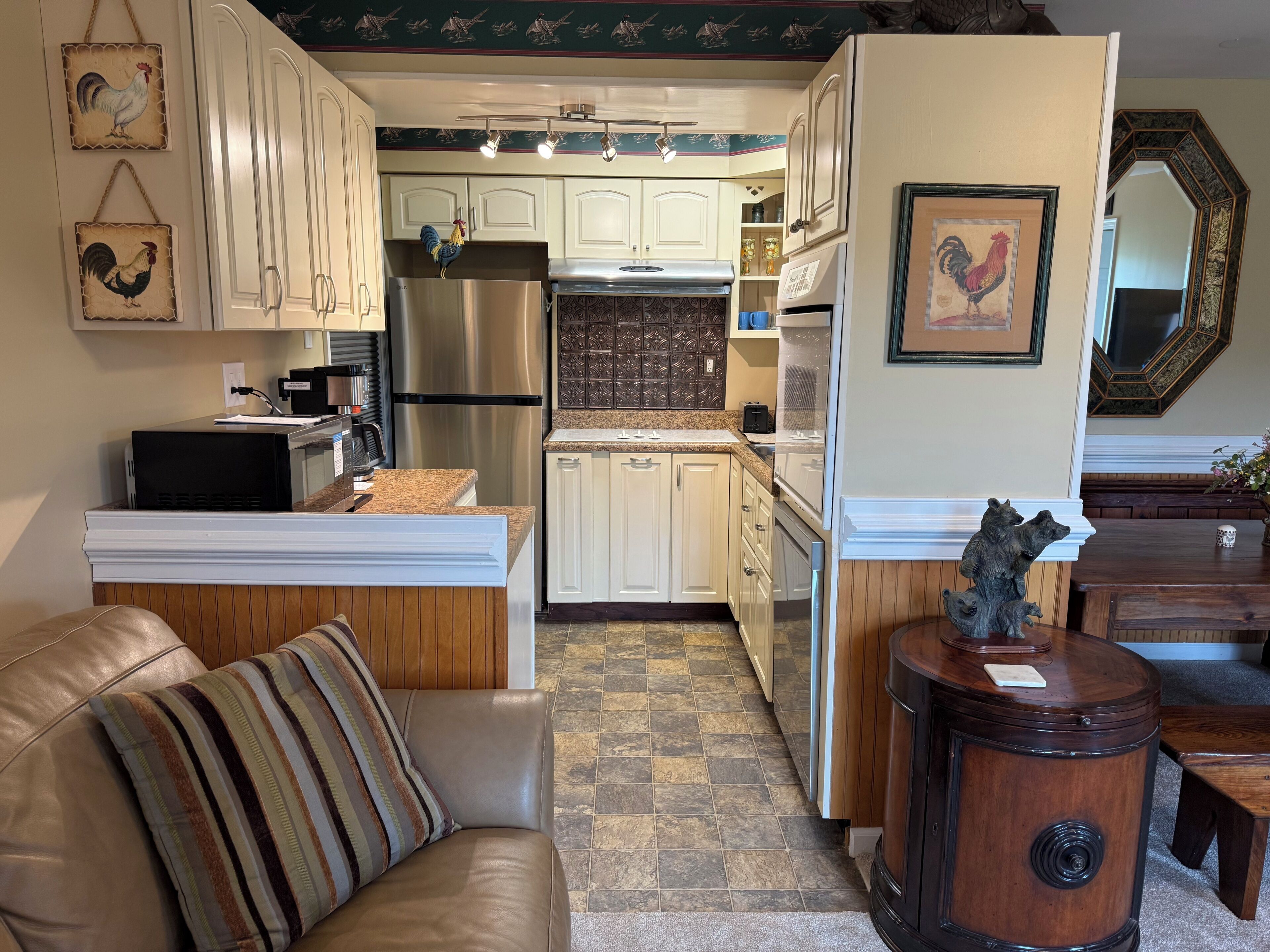 A kitchen with white cabinets, stainless steel appliances, and a striped cushion on a leather sofa.