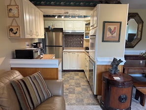 A kitchen with white cabinets, stainless steel appliances, and a striped cushion on a leather sofa.