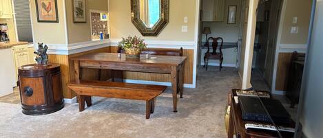 Un comedor con mesa de madera, bancos, un espejo decorativo y una estantería.