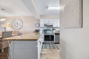 A modern kitchen with white cabinets, a stainless steel oven, and a clock on the wall. - Seaside Beach and Racquet 5216 | BeachFront + Pool (Orange Beach)