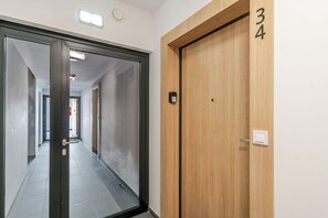 Un couloir avec une porte en bois portant le numéro 34, une porte en verre et un interrupteur sur le mur.