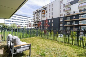 Ein modernes Apartmenthaus mit Balkonen, einem grünen Innenhof und einem Metallzaun.