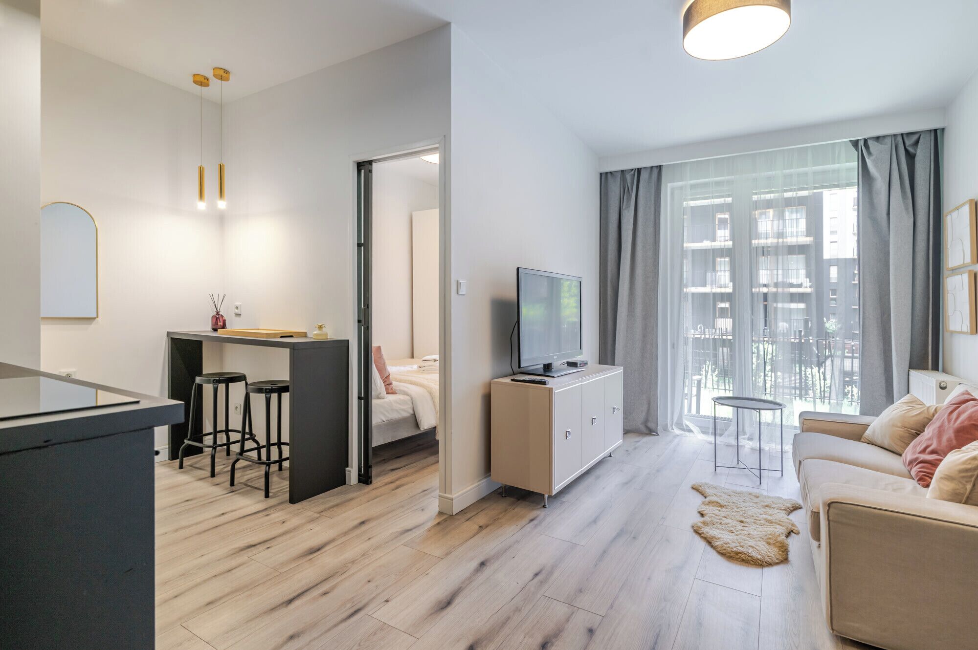 A modern apartment with a kitchenette, a dining area, a living room with a sofa, a TV, and a view of the city.